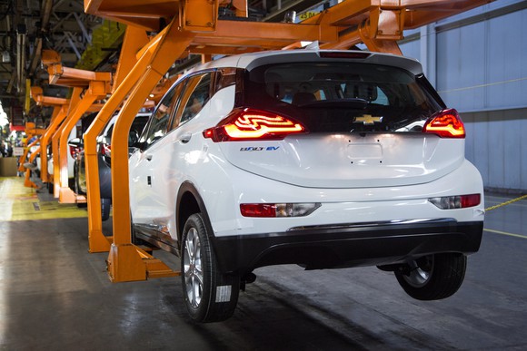 A partially assembled white Chevrolet Bolt EV is shown in an orange tooling cradle on an assembly line. 