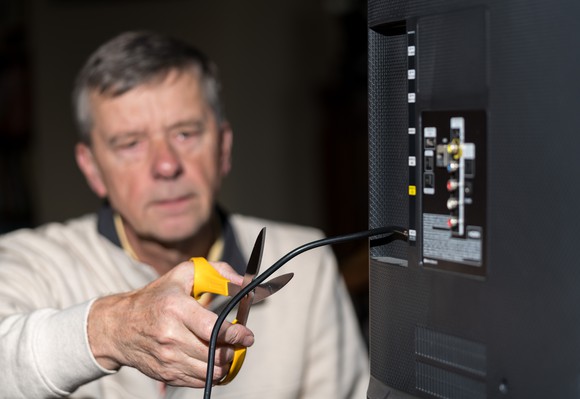 A man cutting the cable cord on his TV with a pair of scissors.
