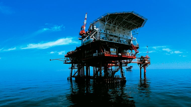 A drilling rig in the ocean with a blue sky in background.