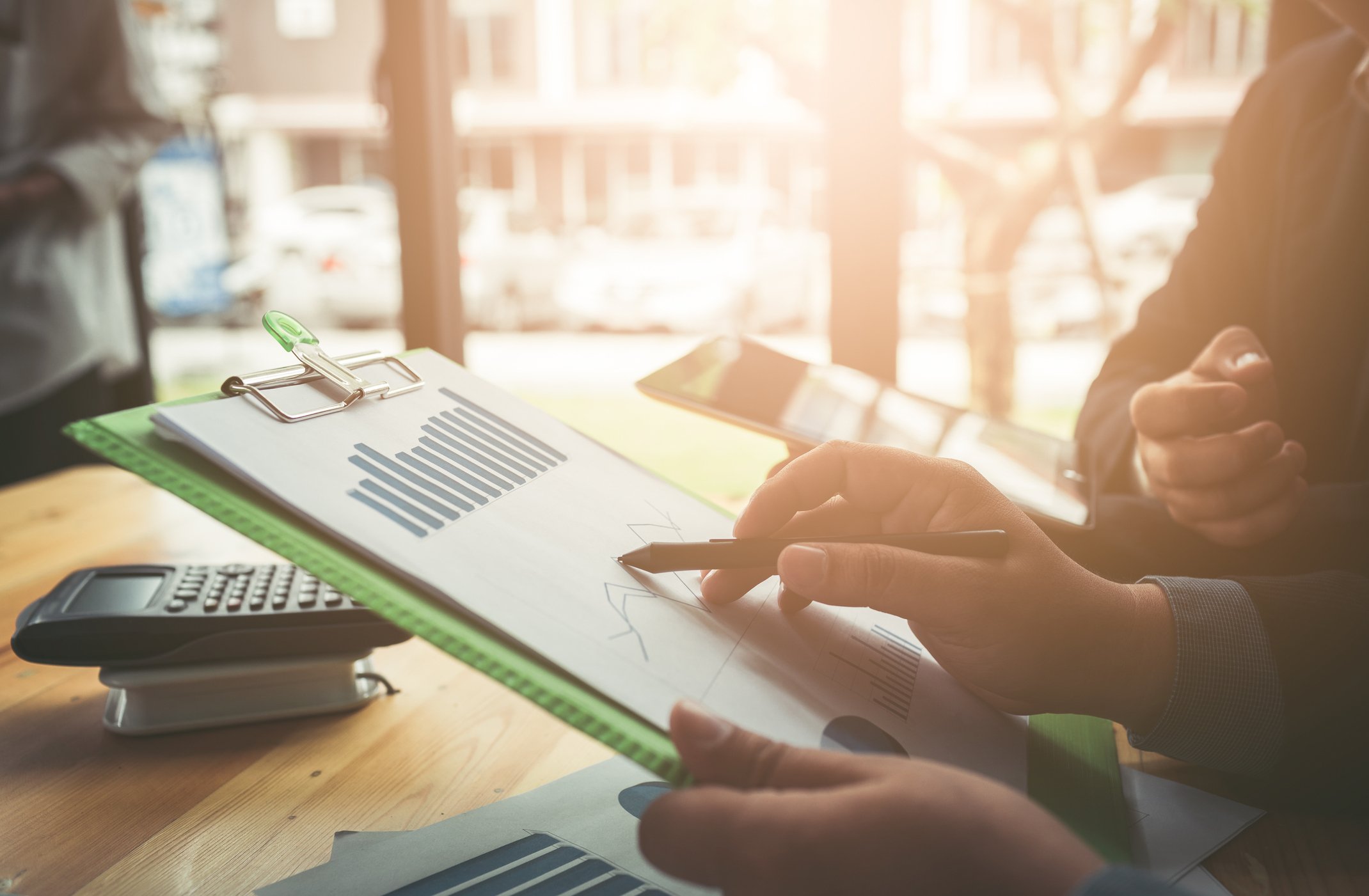 A person in an office pointing to a bar chart on a clipboard.