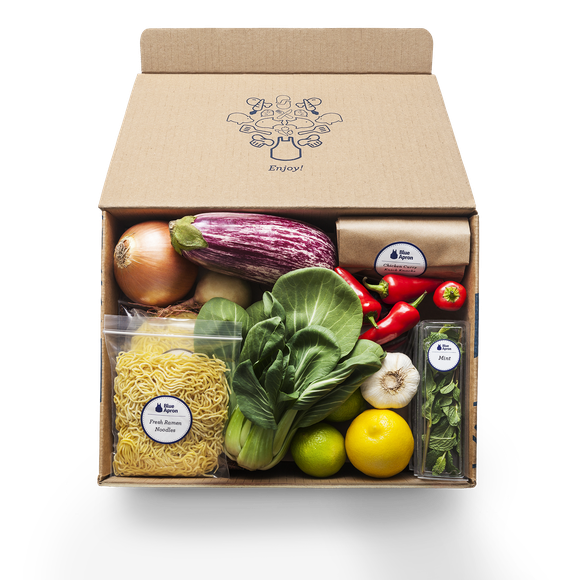 A sample box from Blue Apron containing various vegetables and a pack of noodles.