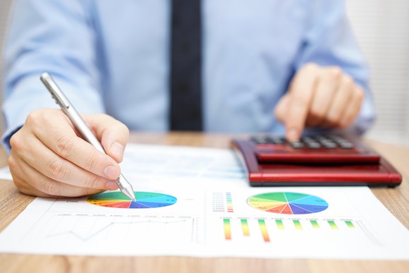 A man marking on a pie chart with one hand while operating a calculator with the other