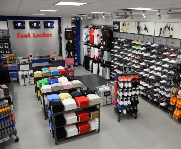 The interior of a Foot Locker store. Shoes are on the shelves, and apparel is on display in the center of the store.