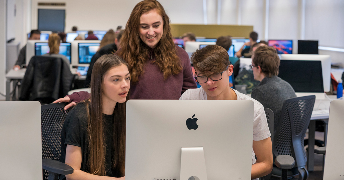 Three people using a desktop Mac computer.