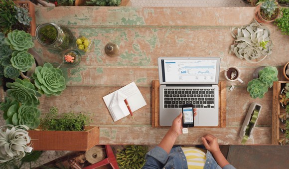 Overhead view of a Square mobile reader, dashboard on a laptop, and a notebook.