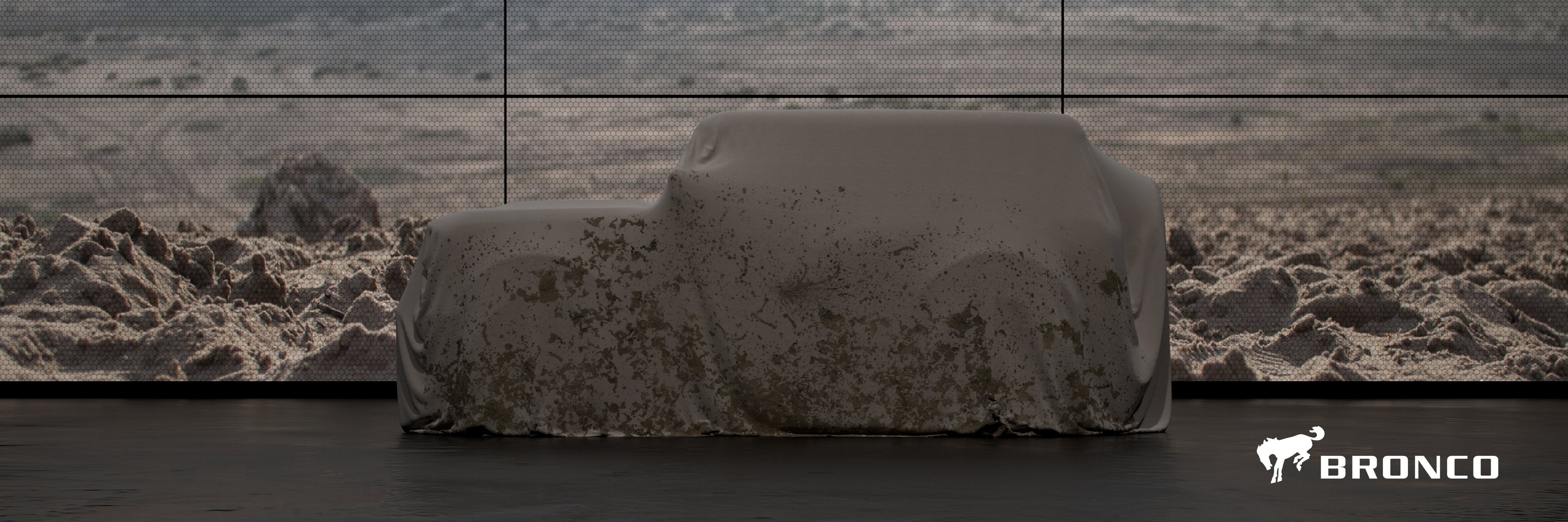 An angular SUV is shown under a cover in front of a rocky background