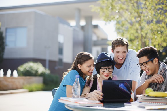 Group of college students gathered around a laptop.