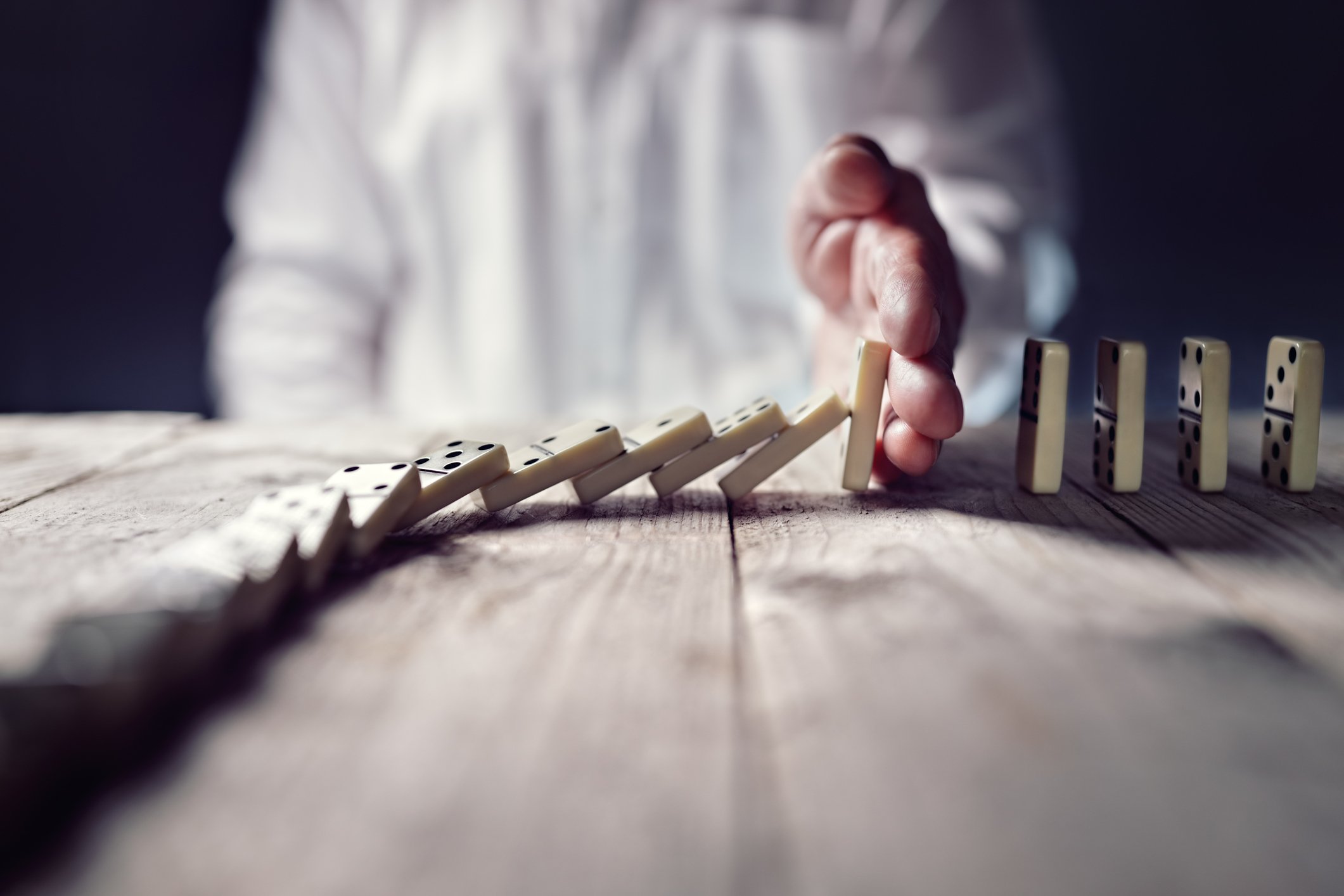A businessman stops a row of dominoes from falling.