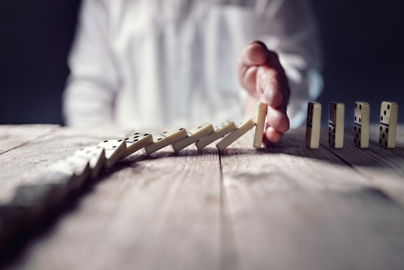A businessman stops a row of dominoes from falling.
