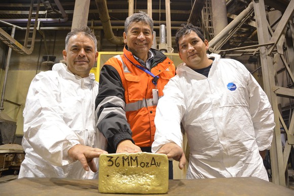 Three people standing behind a huge bar of gold.