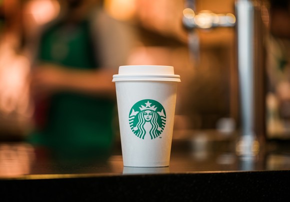 A Starbucks cup sits on a table with blurred background.