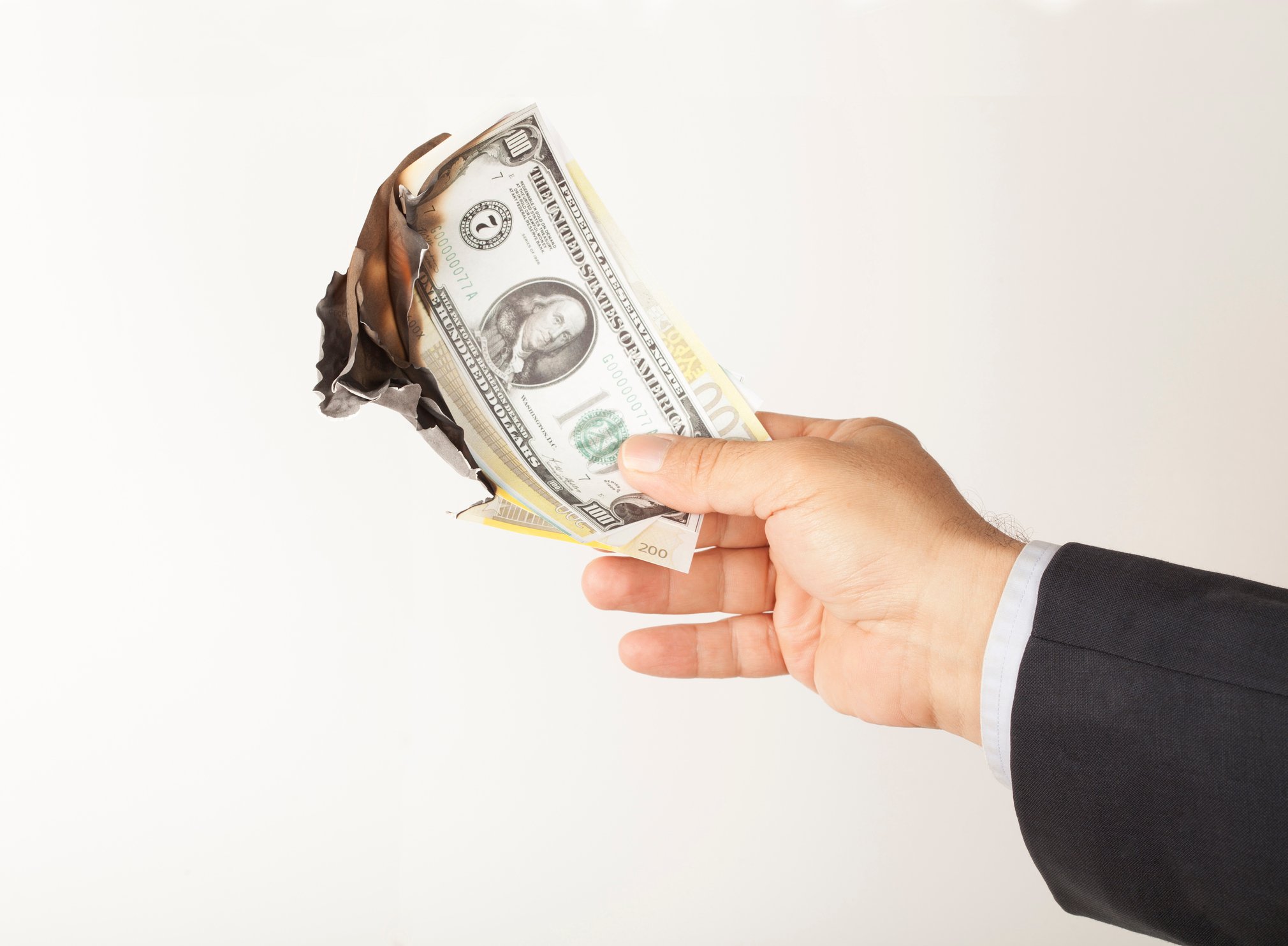 A man's hand holding a pile of burning $100 bills