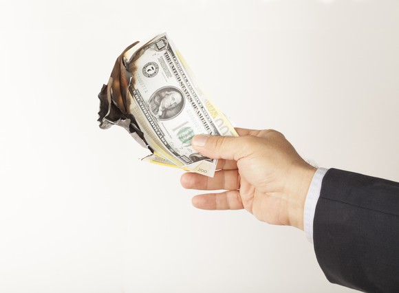 A man's hand holding a pile of burning $100 bills