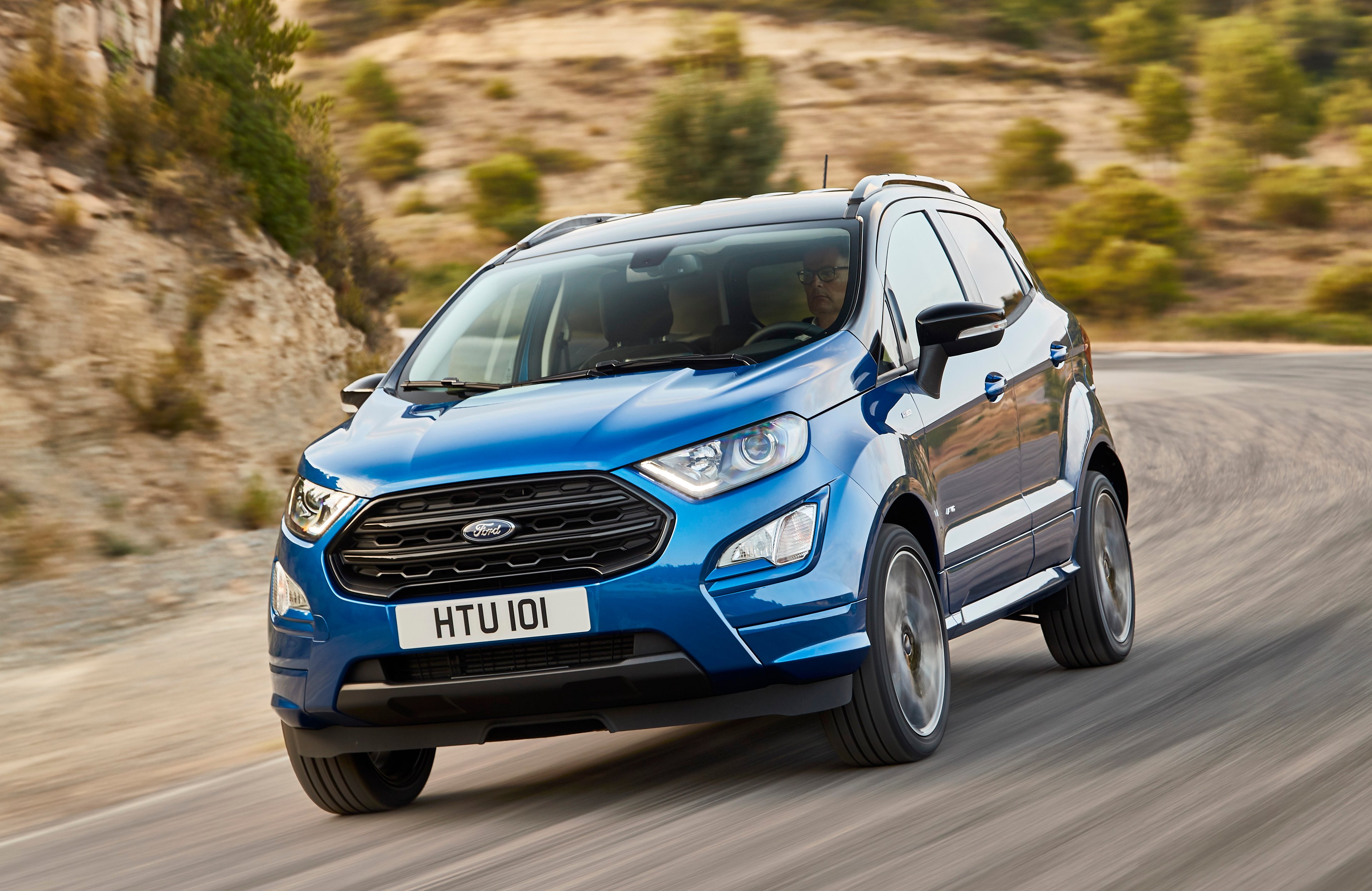 A blue 2018 Ford EcoSport, a small SUV, with UK license plate, on a country road.