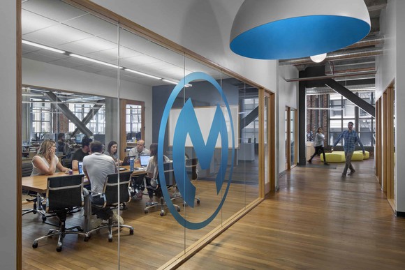 Hallway and glass-walled conference room with large blue M logo on the window.