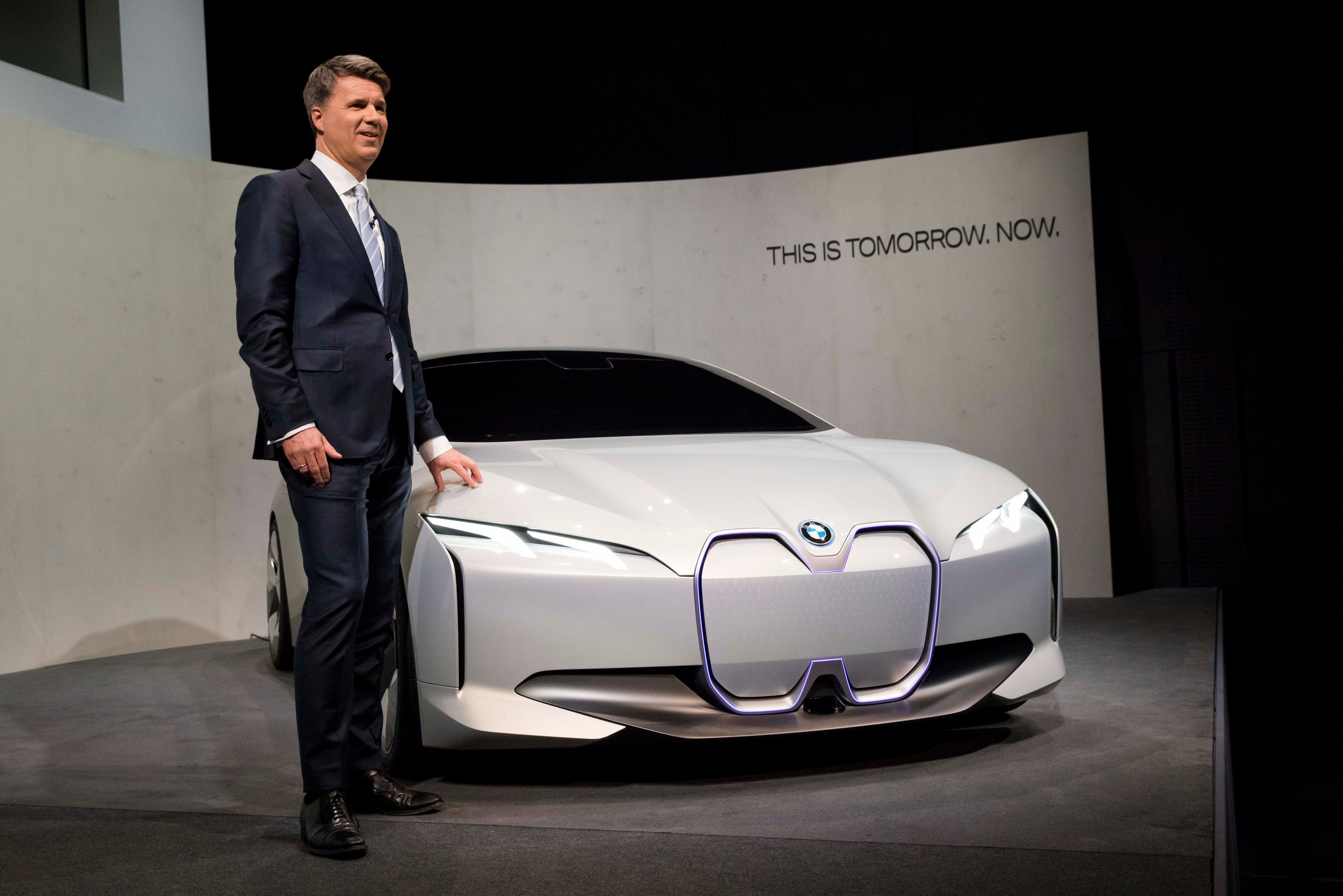CEO Harald Krueger standing next to a low-slung white sedan, the BMW Vision Dynamics show car.