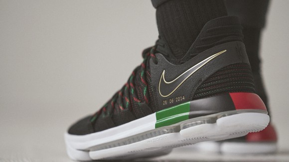 Black, red, green, and white Nike Durant Equality Sneaker on someone's feet.