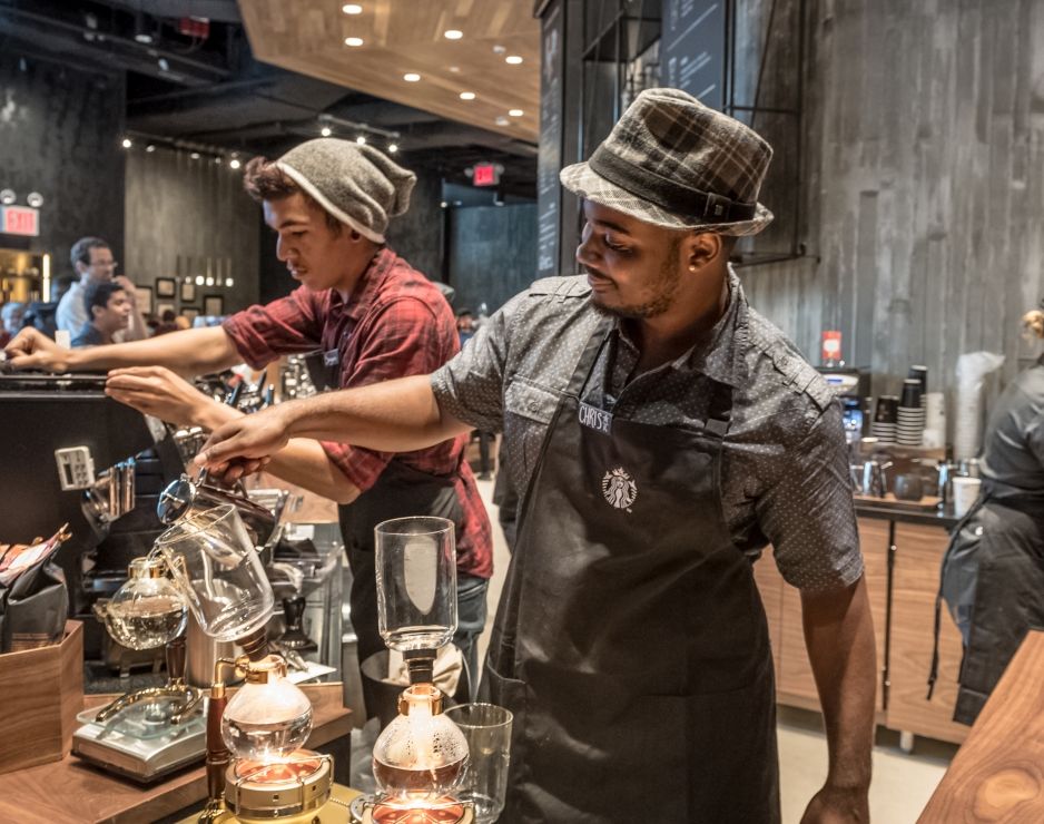 Two male Starbucks baristas prepare beverages at its Reserve roastery.