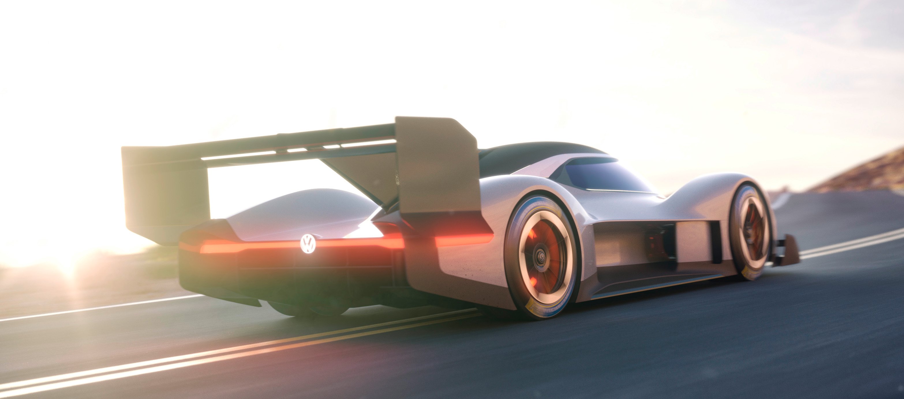 The VW I.D. R Pikes Peak, a low-slung grey racecar with a big rear wing, is shown on a mountain road.