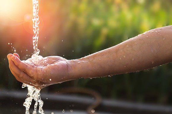 A person putting their hand under a tap outside.