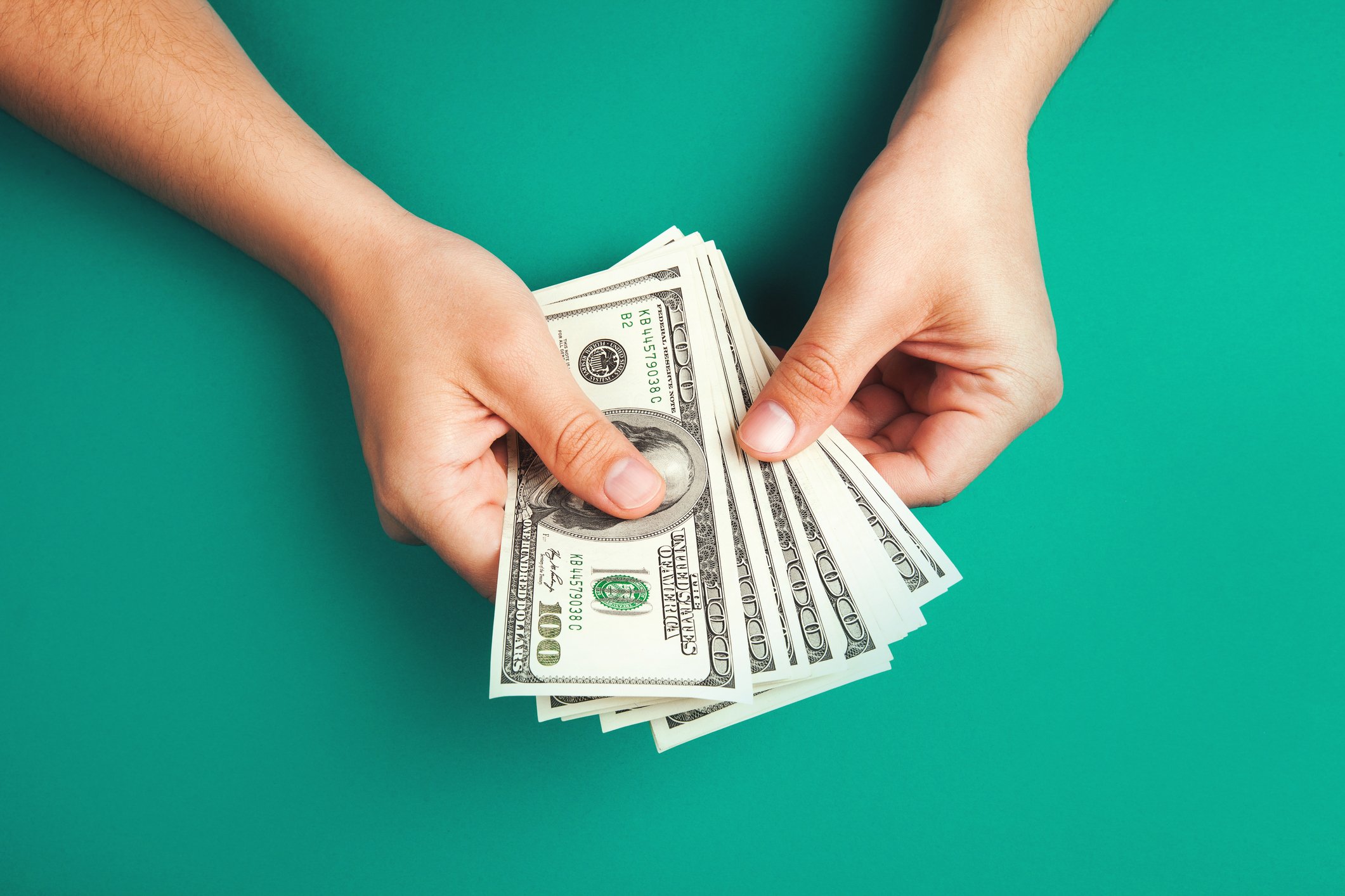 Person holding out 100-dollar bills on a green background