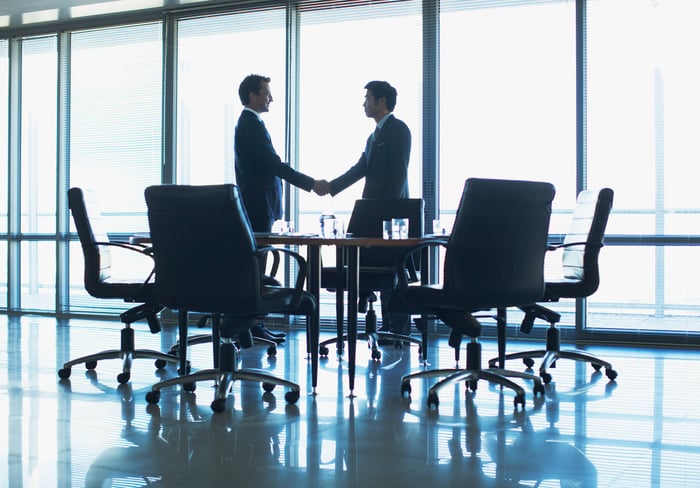 Two people shaking hands in a conference room.