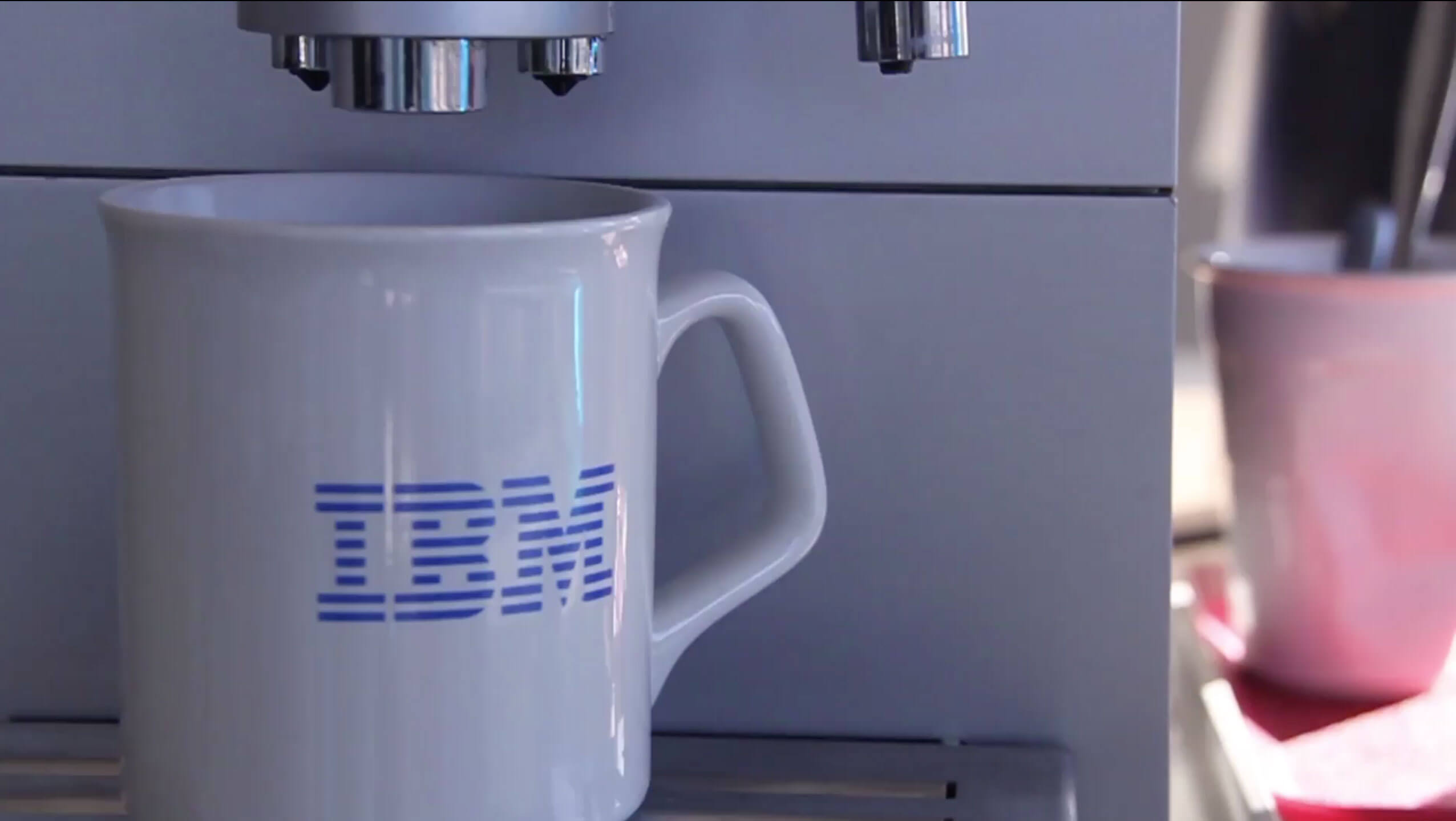 White coffee mug with IBM logo on it, underneath a coffee dispenser.