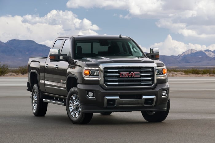 Black GMC pickup truck on pavement in front of a mountain landscape.