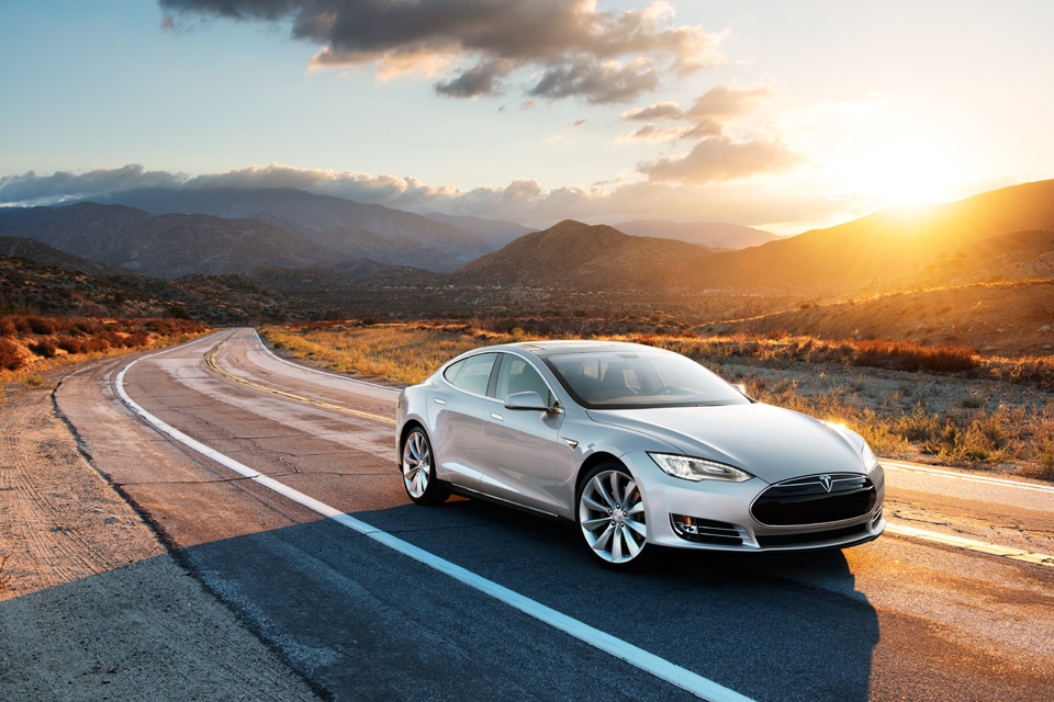A silver Tesla Model S driving, with hills in the background