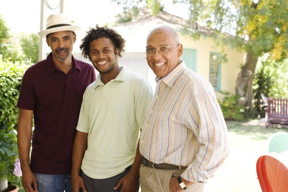 Three men standing next to each other and smiling in front of a house.