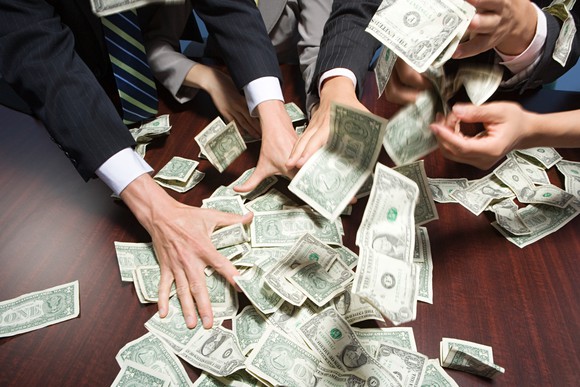 People in business attire grabbing cash scattered on top of a table