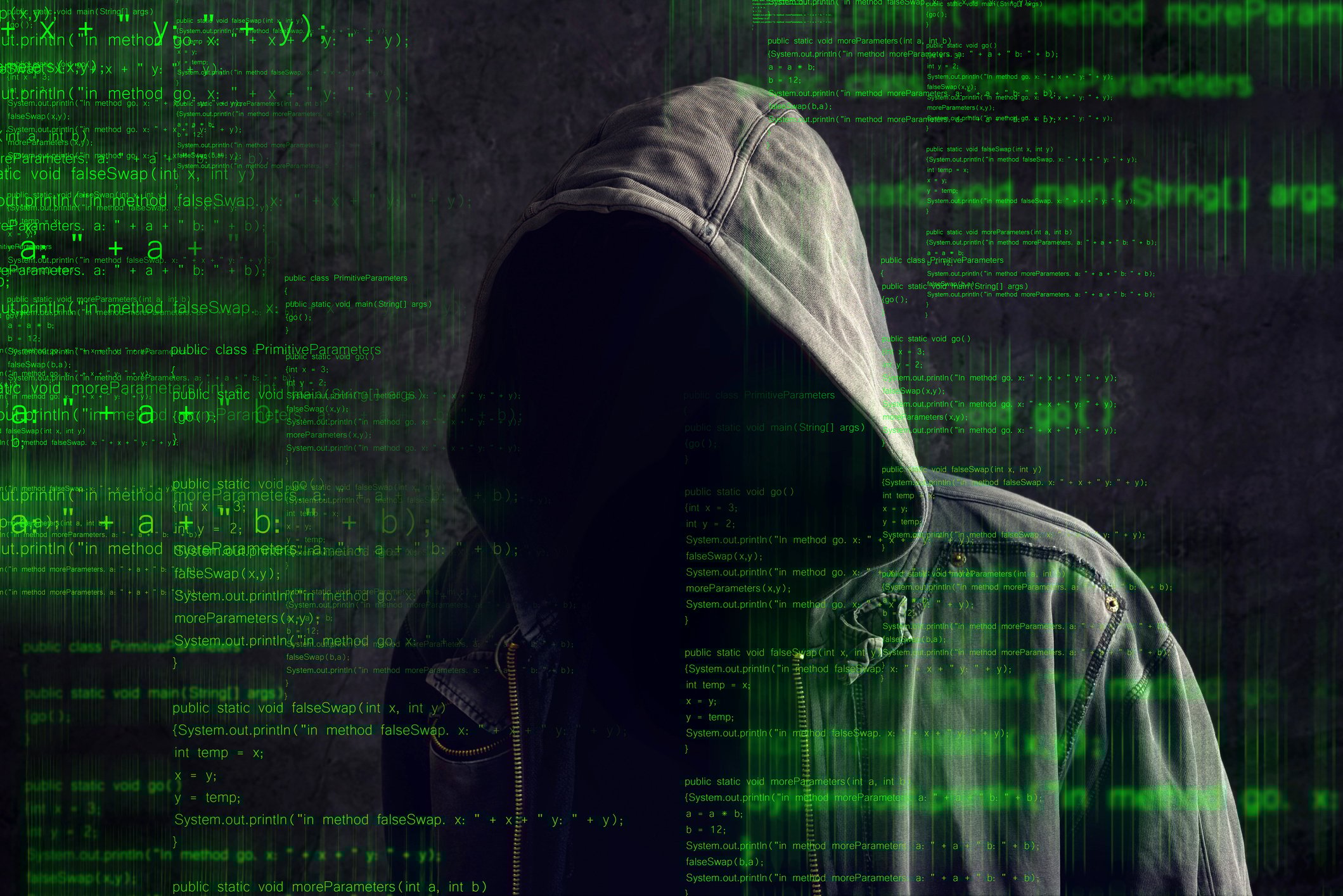 A shadowy figure in a dark hoodie, behind computer code shown in green text