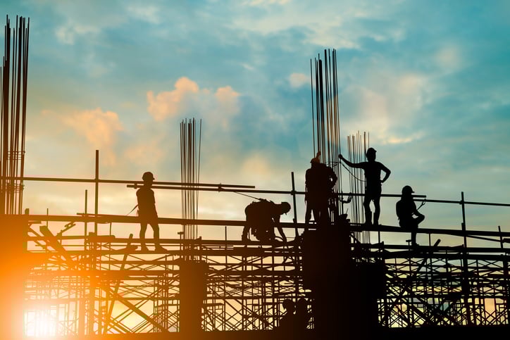 A silhouette of construction workers building a large facility.