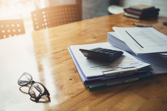 Paperwork, a calculator, and reading glasses on a desk.