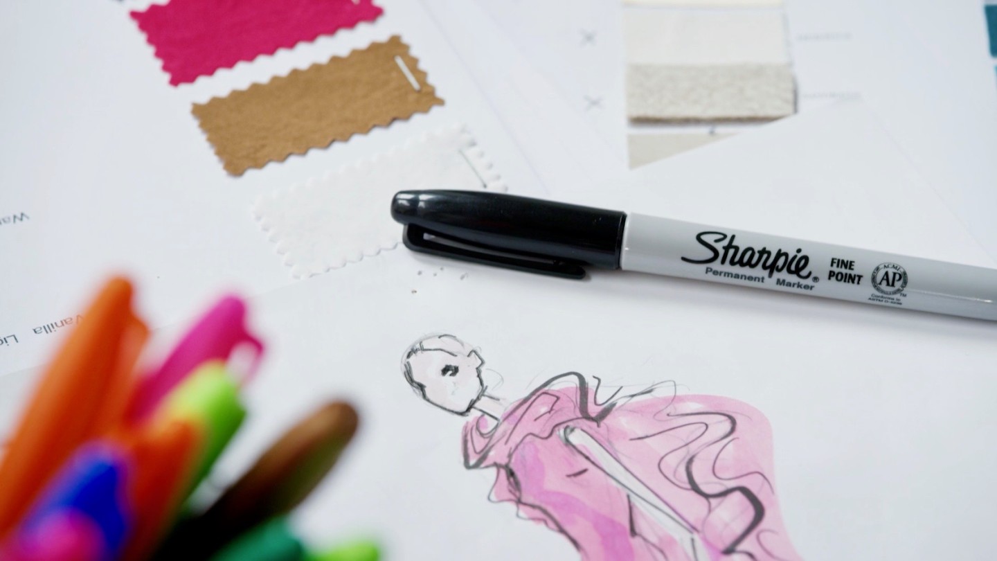 Black Sharpie marker on piece of paper showing a clothing sketch, next to cloth swatches