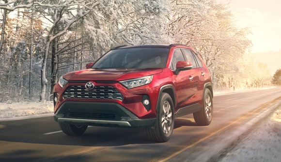 A red 2019 Toyota RAV4, a compact SUV, on a road next to a line of snow-covered trees.