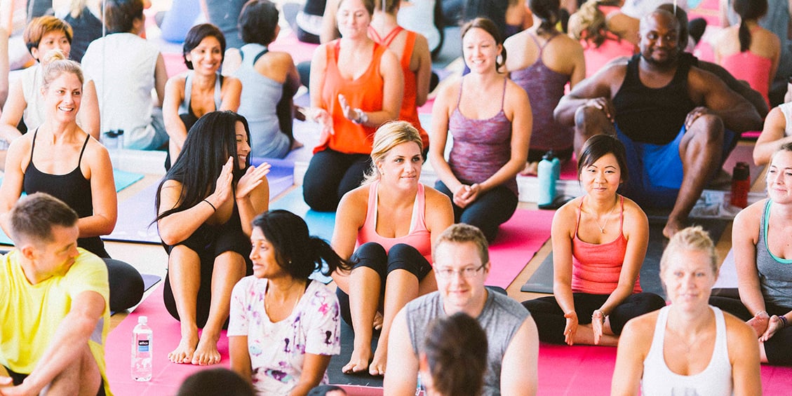 Group of men and women sitting on mats at a yoga class.