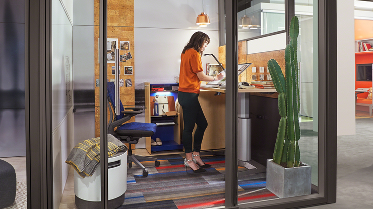 Employee at standing desk in a contemporary, glass cubicle office setting.