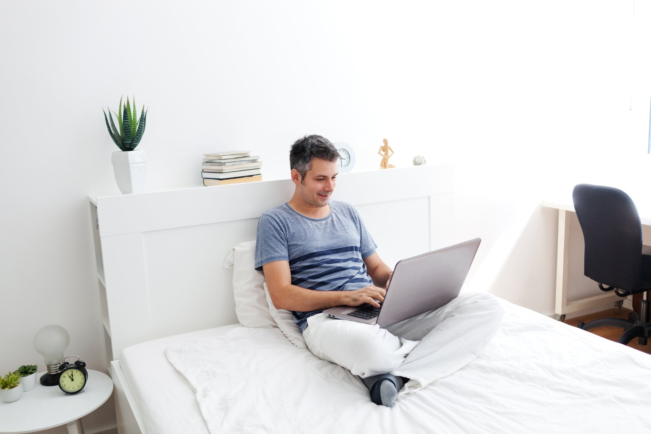Man sitting in bed while working on a laptop in bed