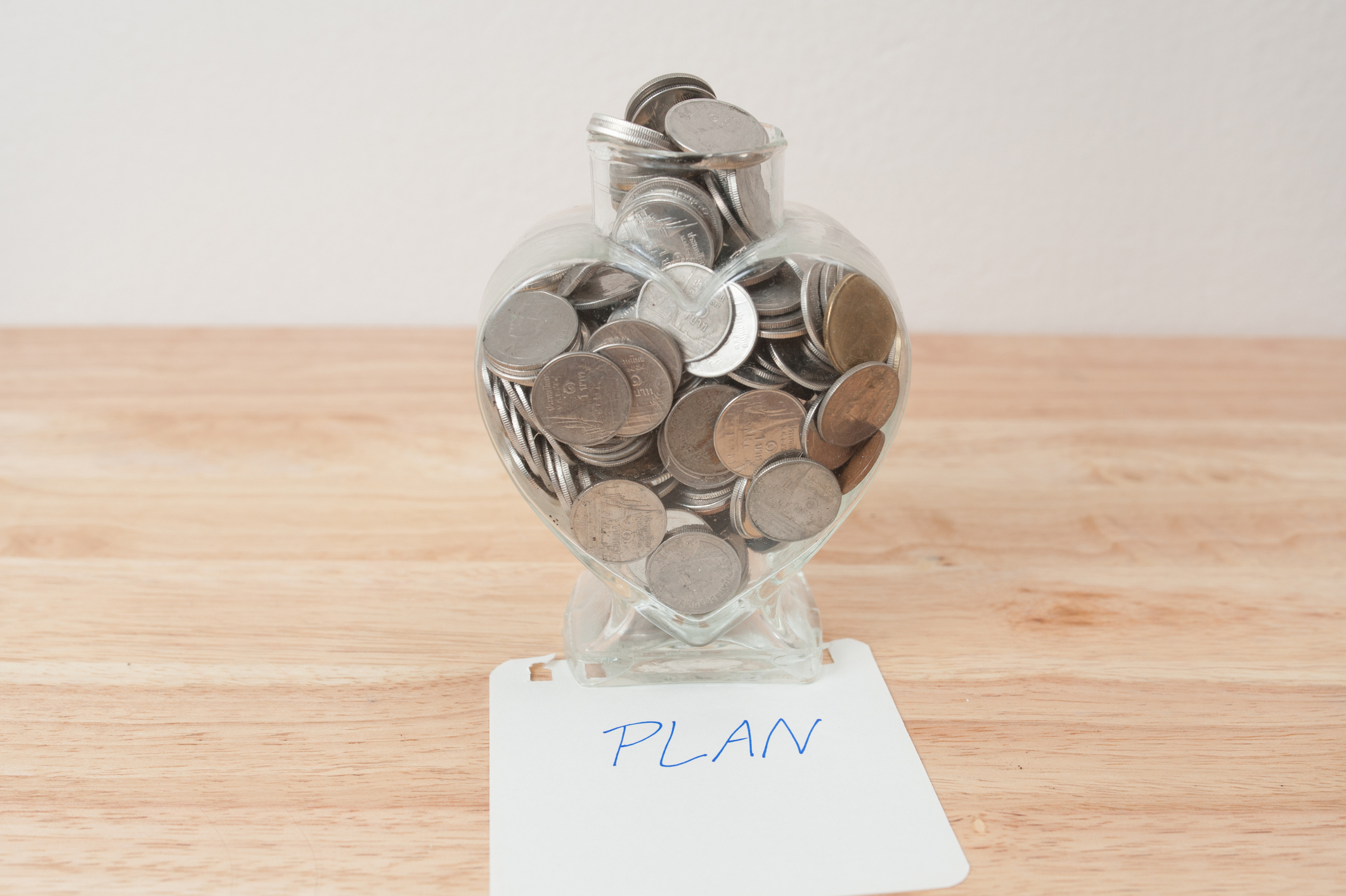 Jar of coins sitting on a wooden table with a piece of paper under them with "PLAN" in blue letters.