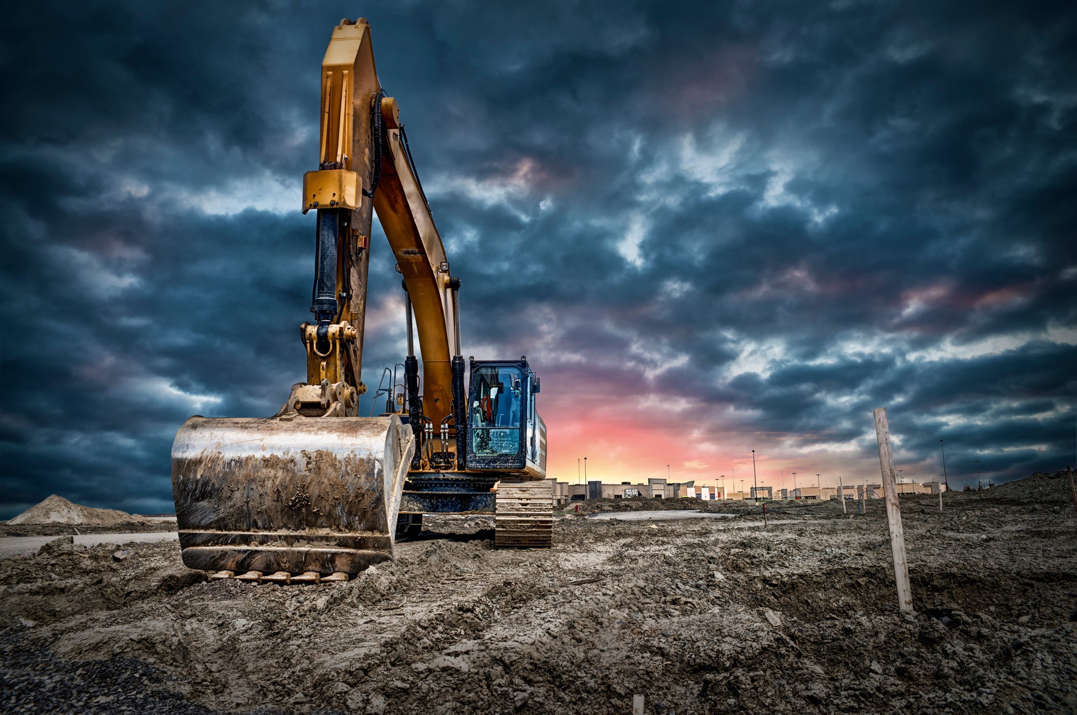 A backhoe on a construction site with a cloudy sky and setting sun