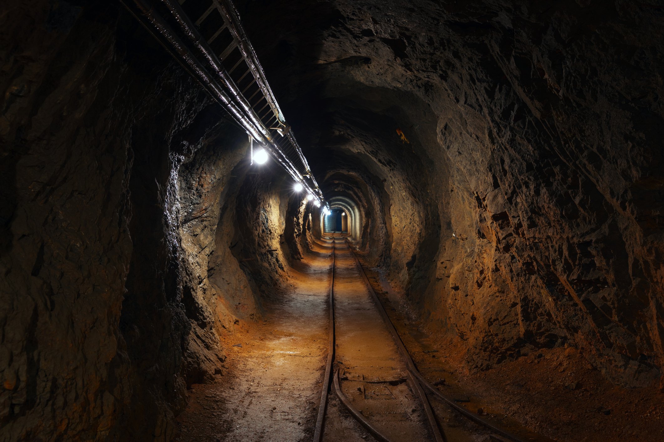 An underground mine passage with rails and lights.