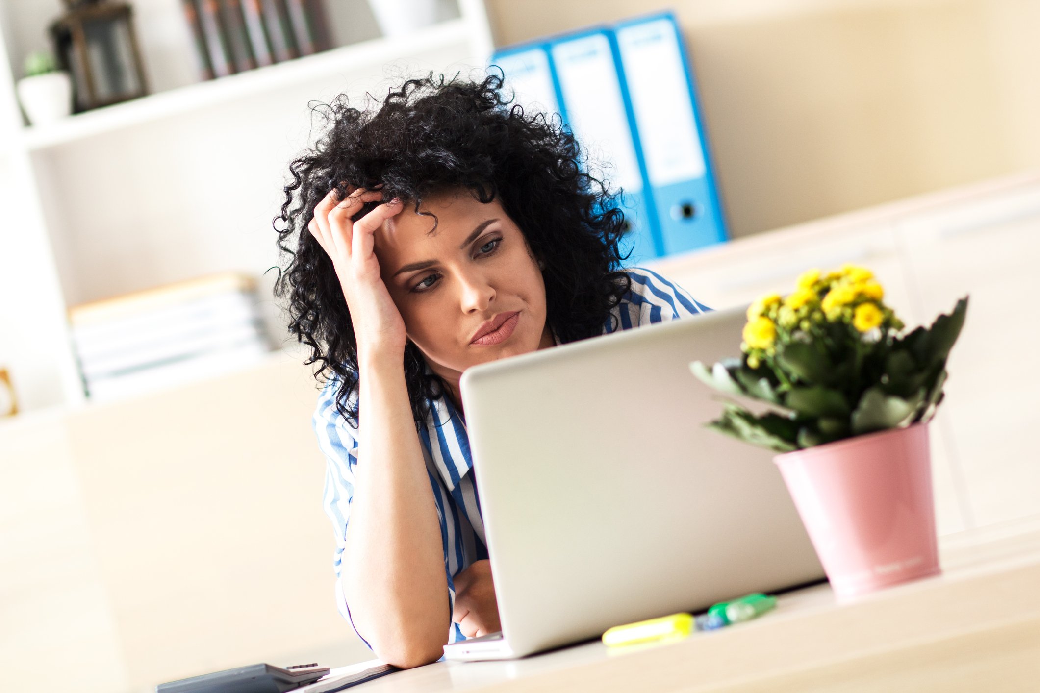 A frustrated women holding her hand to her head while reading an article on her laptop.