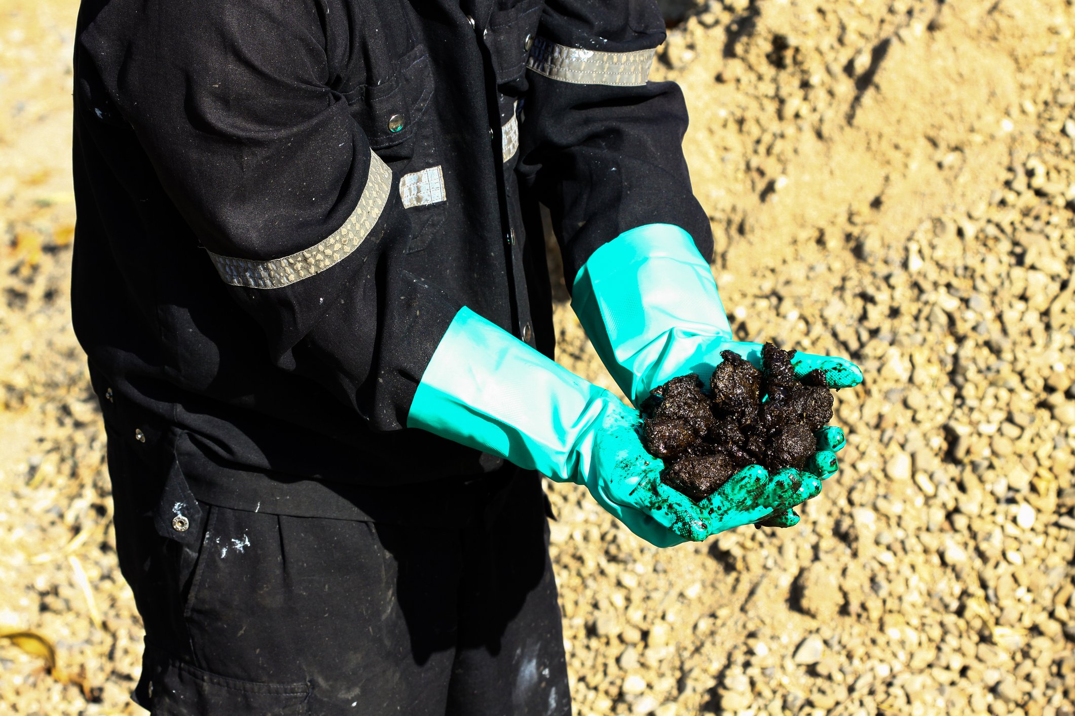 A worker's gloved hands showing an oil sands sample from a mine.