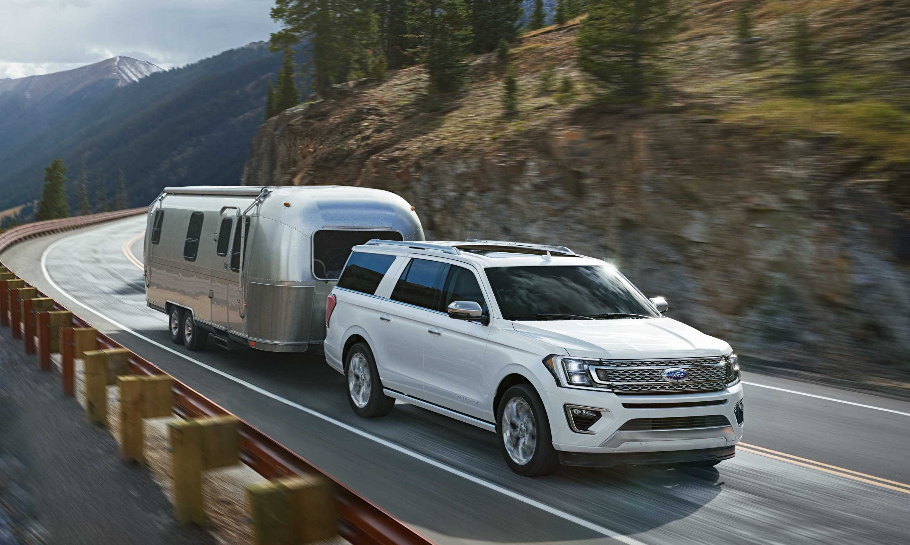A white 2018 Ford Expedition, a full-size truck-based SUV, pulling an Airstream trailer on a mountain road. 