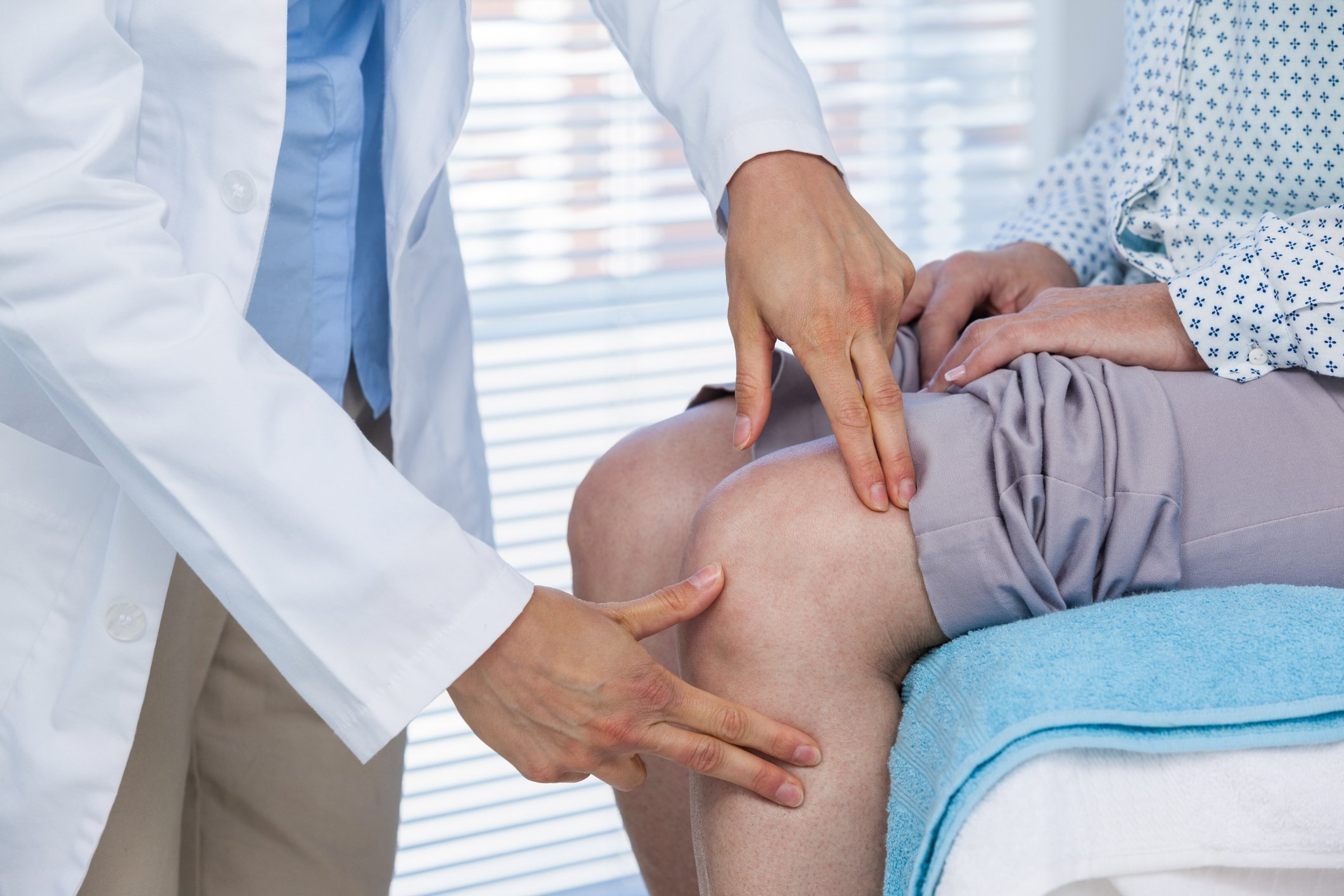 A standing doctor examining a seated patient's knee
