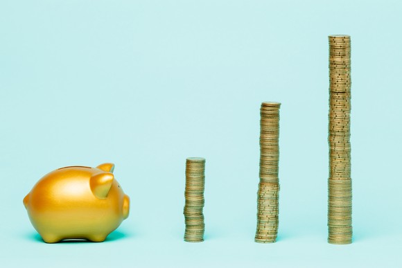 A golden piggy bank standing in front of three stacks of golden coins, ascending in size from left to right.