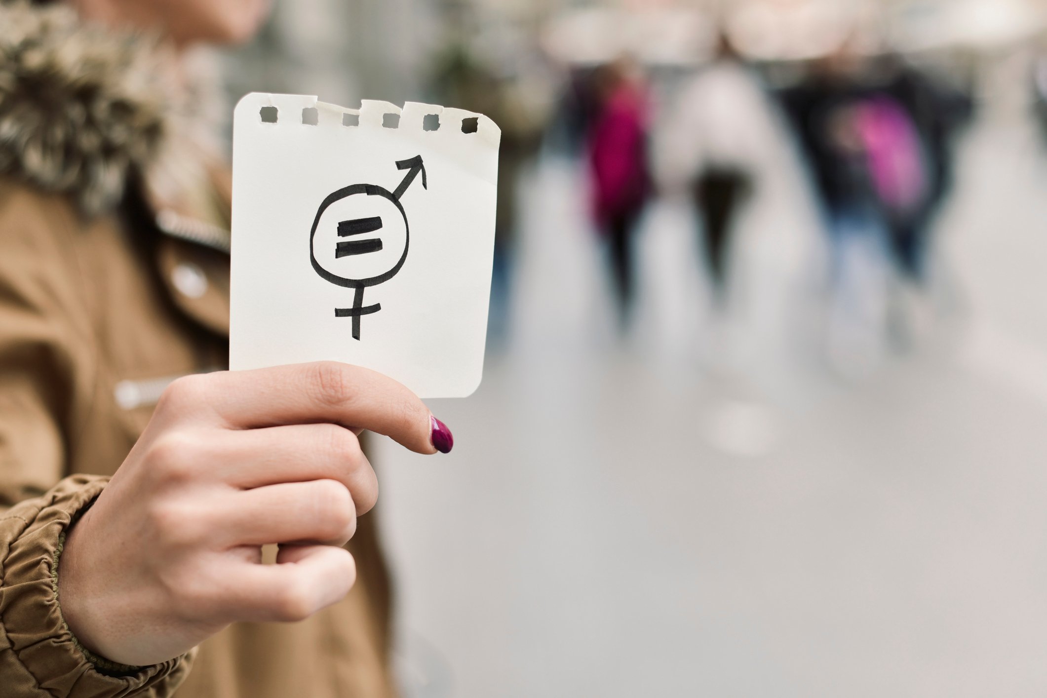 A woman holds a symbol for gender inequality. 
