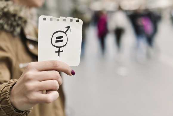 A woman holds a symbol for gender inequality. 