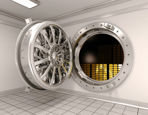 A bank vault door is open revealing stacks of gold bars inside.